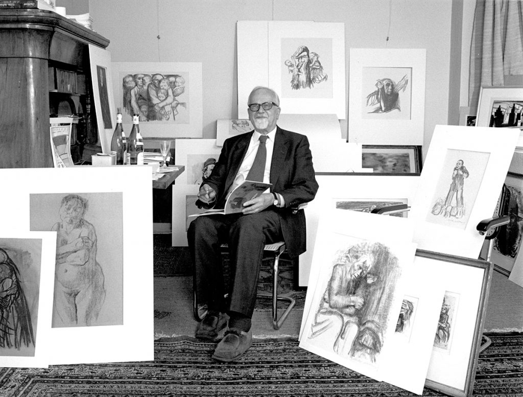 Black and white photograﬁe of Hans Pels-Leusden. He sits surrounded by Kollwitz works placed around him for the photo. He wears a suit and smiles at the camera. In his left hand he holds a cigar. In his right hand he holds an open catalog. The Kollwitz works are for the most part easily recognizable.