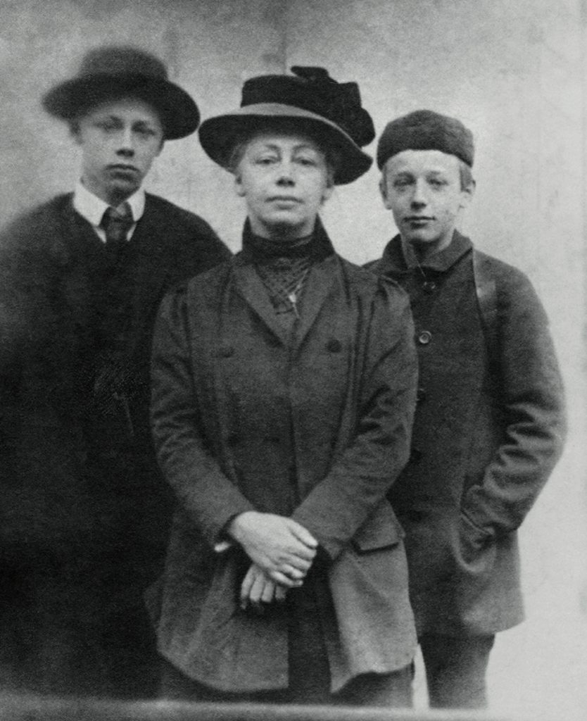 Käthe Kollwitz steht in der Mitte und trägt einen Hut. Ihre beiden noch minderjährigen Söhne stehen an ihrer Seite. Der ältere Bruder Hans Kollwitz (1892-1971) steht auf der linken Seite; der jüngere Bruder Peter Kollwitz (1896-1914) steht auf der rechten Seite.