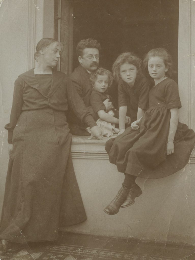 Die historische schwarz-weiß-Aufnahme zeigt ein Familienporträt. Zu sehen sind das Ehepaar Georg und Lisbeth Stern, die gemeinsam mit ihren Kindern an einem offenen Fenster für ein gemeinsames Foto posieren.