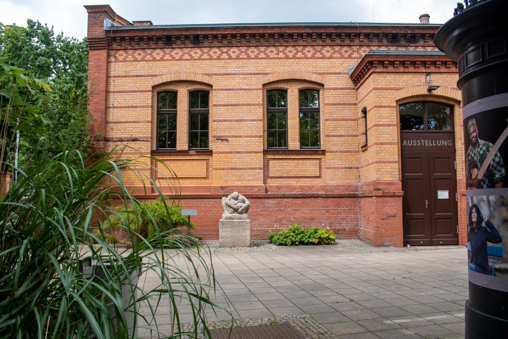 Eine Fotografie aus dem Jahr 2021 vom Hof des Museum Pankow. Vor einem roter Backsteingebäude steht die Nachbildung der Plastik „Mutter mit zwei Kindern“.